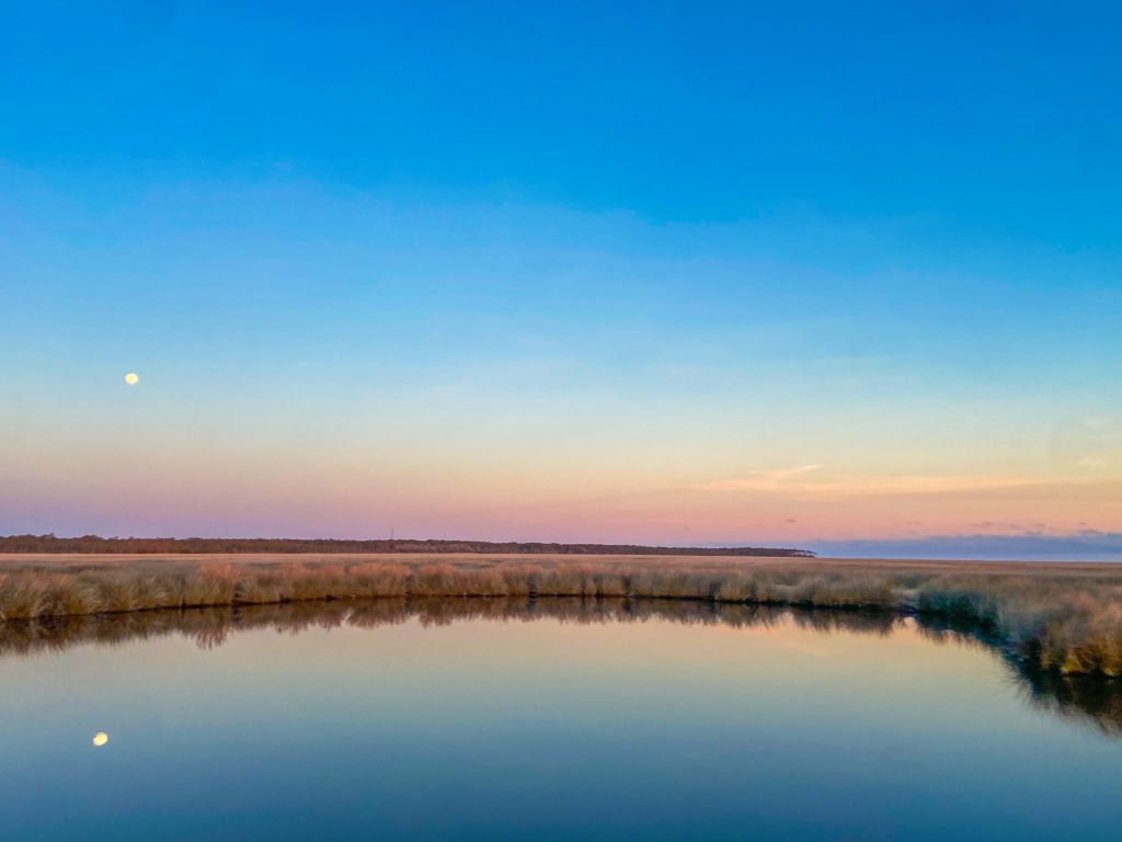 Coastal marsh and calm water at sunset near Wilmington, North Carolina, with the moon reflected in the water.
